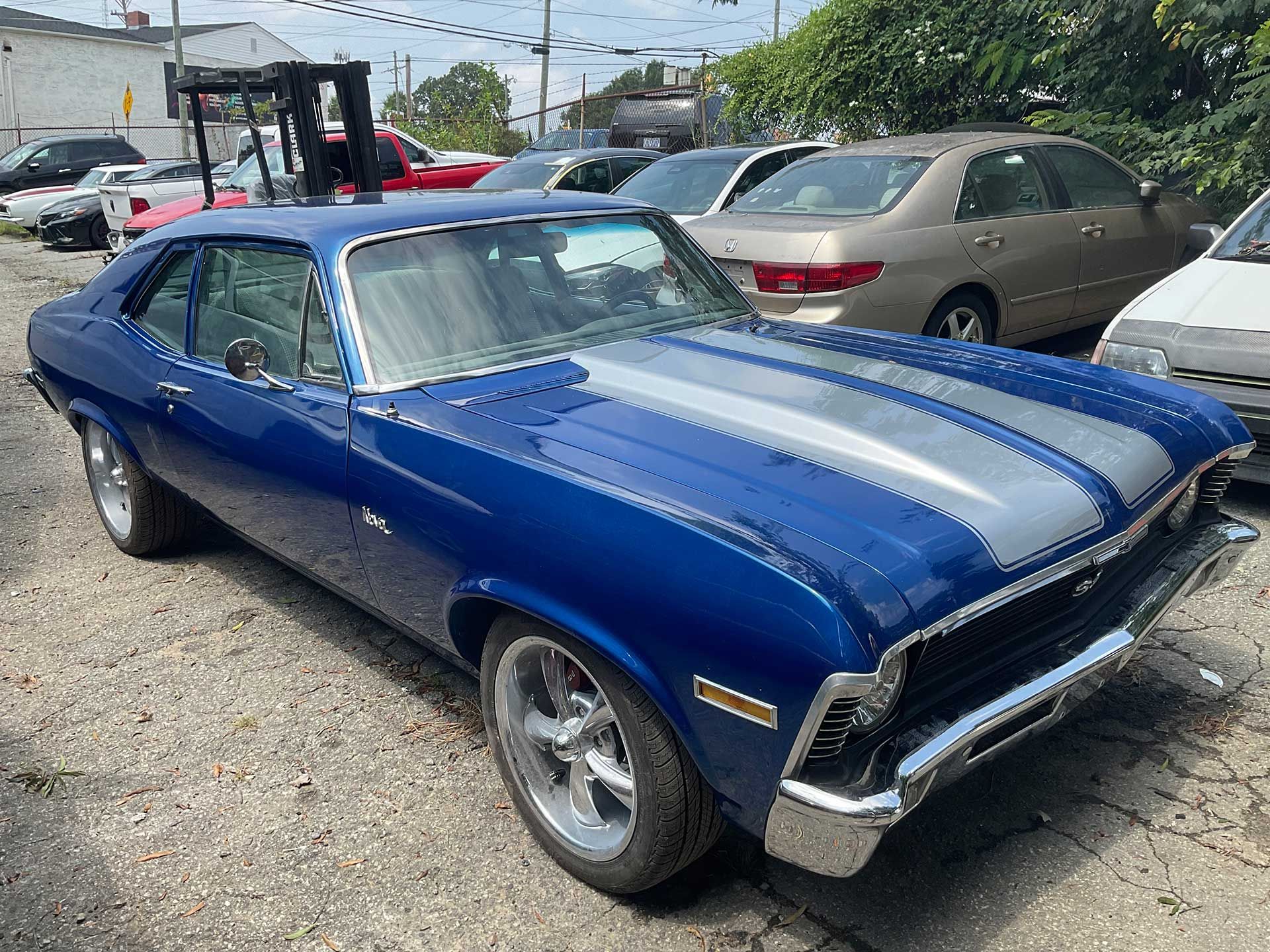 A blue car with a silver stripe on the hood is parked in a parking lot