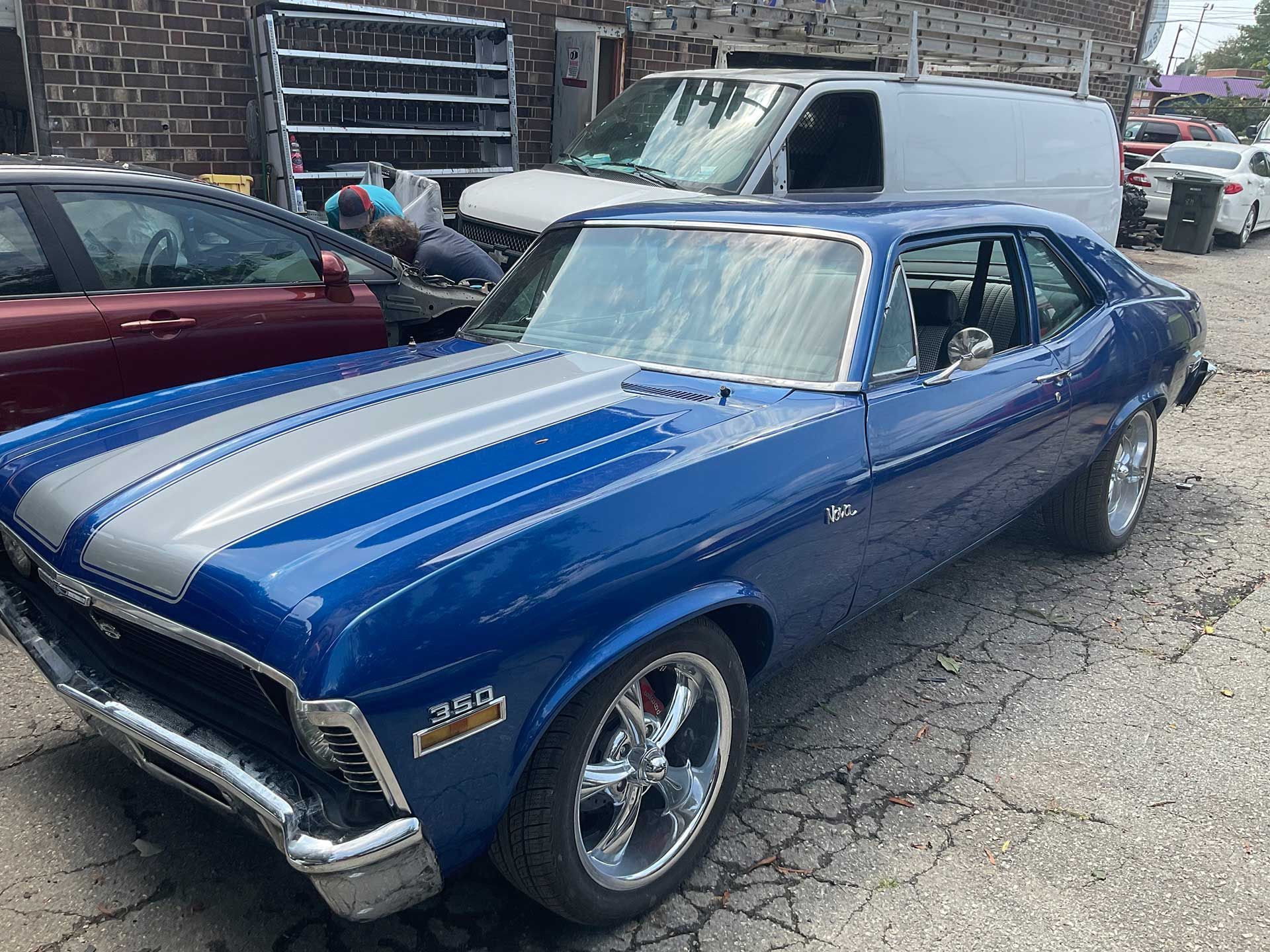 A blue car with silver stripes is parked in front of a building