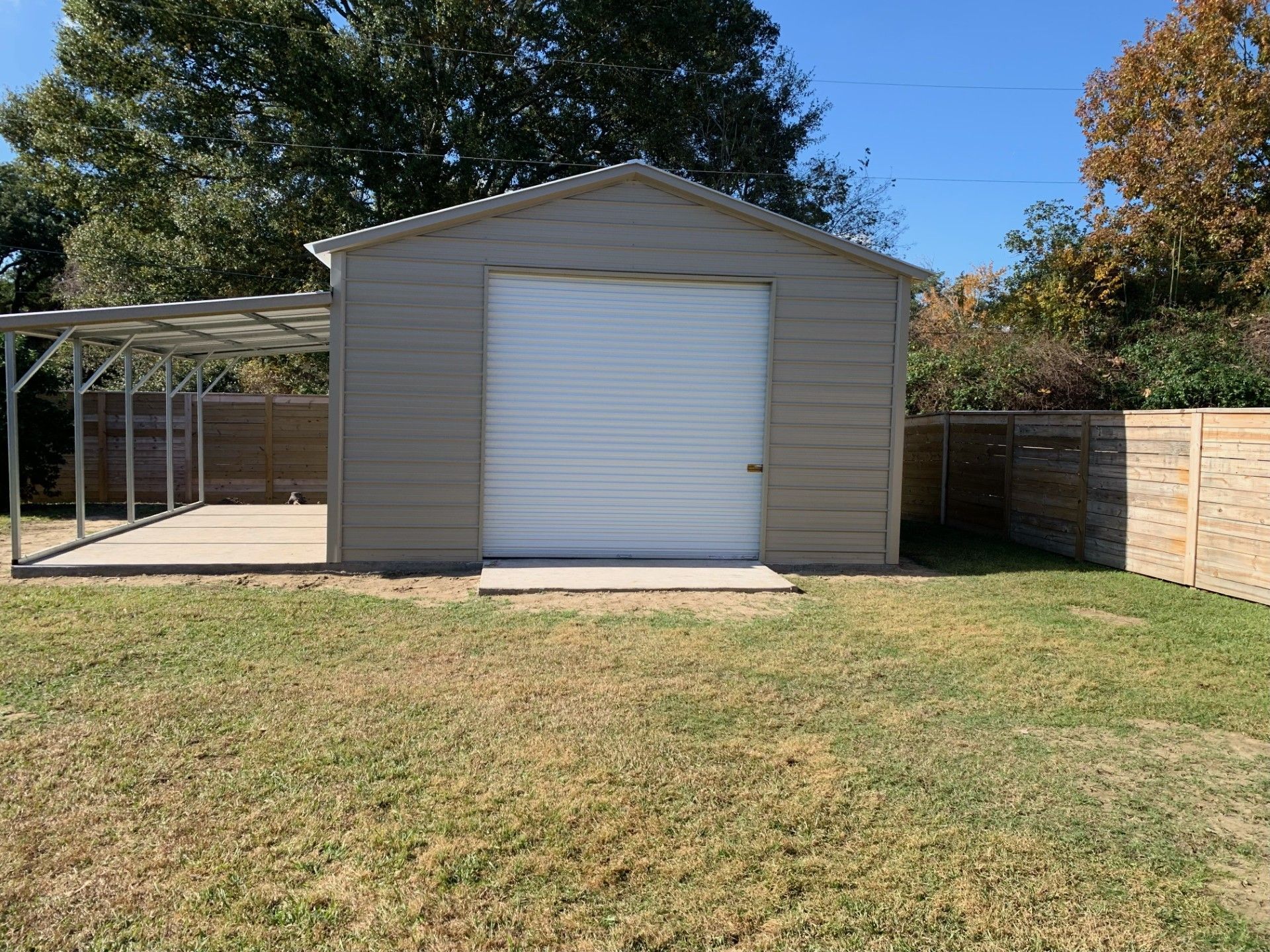 A garage with a white door and a carport in the backyard.