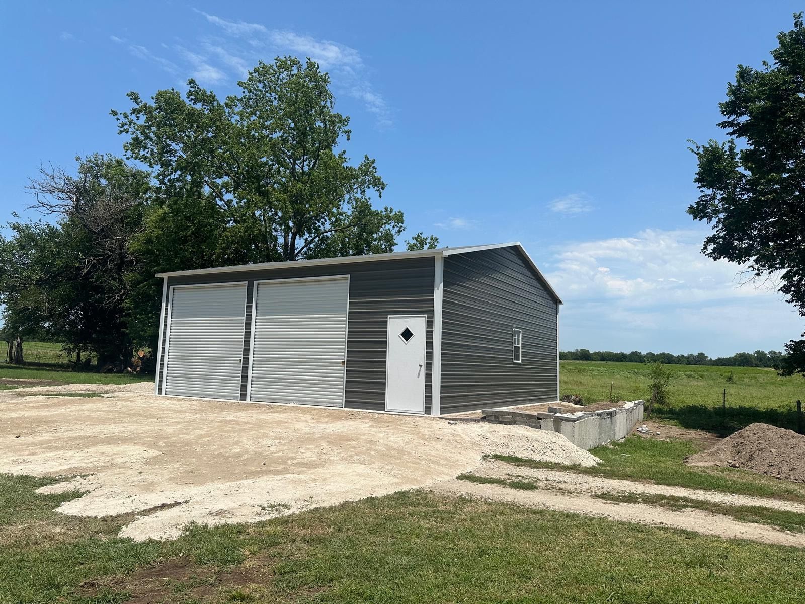 A garage with two garage doors is sitting in the middle of a grassy field.