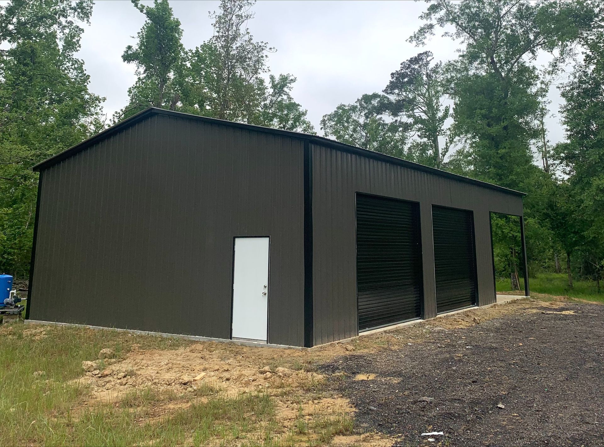 A large metal building with two garage doors is sitting in the middle of a grassy field.