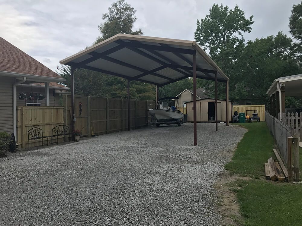A carport with a boat parked underneath it in front of a house.
