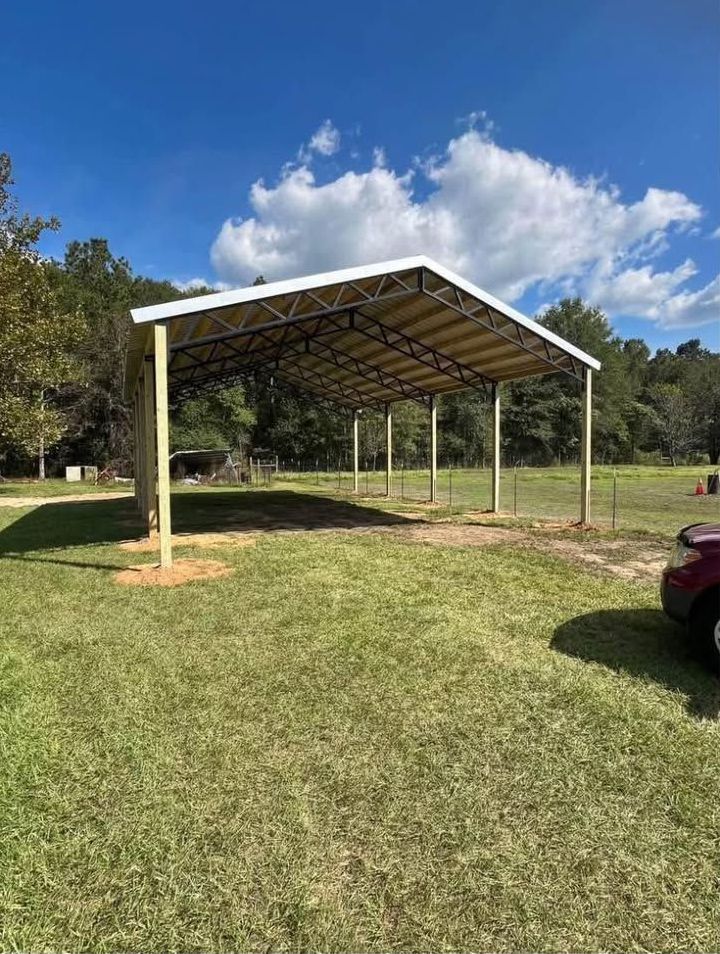 A car is parked under a canopy in a grassy field.