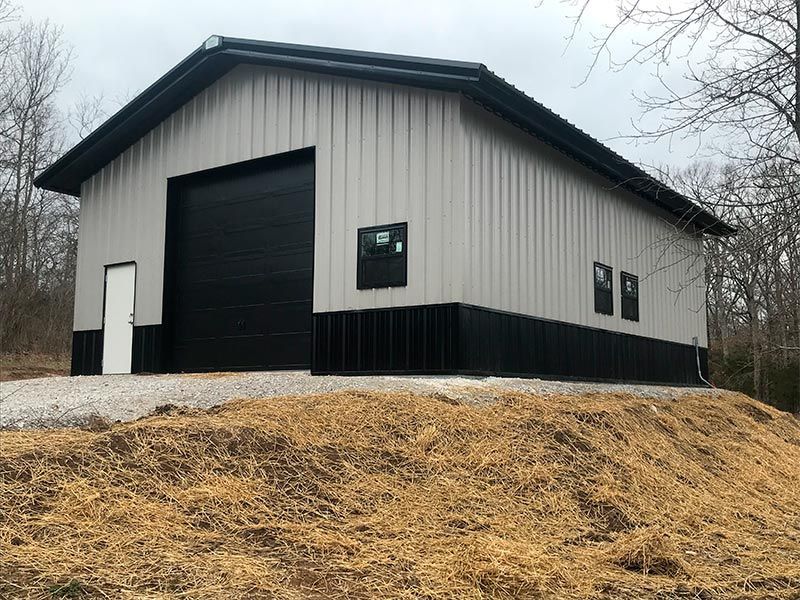 A large metal building with a black garage door is sitting on top of a hill.