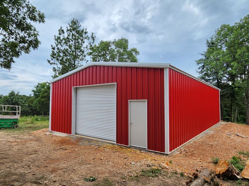 A red metal building with a white door is sitting in the middle of a dirt field.