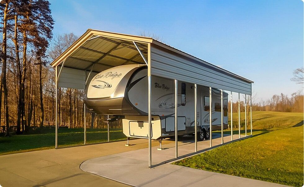 RV parked under a steel carport with a concrete driveway and grass on either side, in a sunny, outdoor setting.