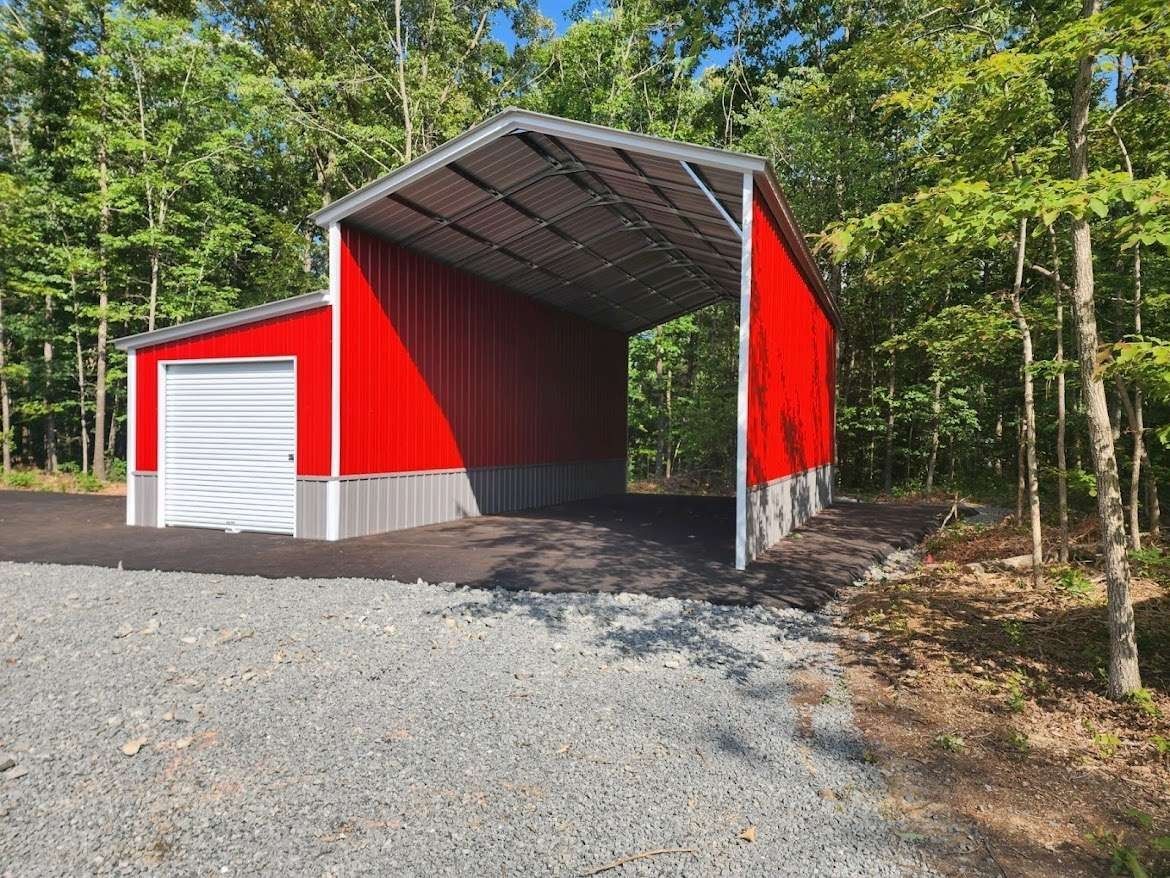 Red and white metal building with a carport in a wooded area.