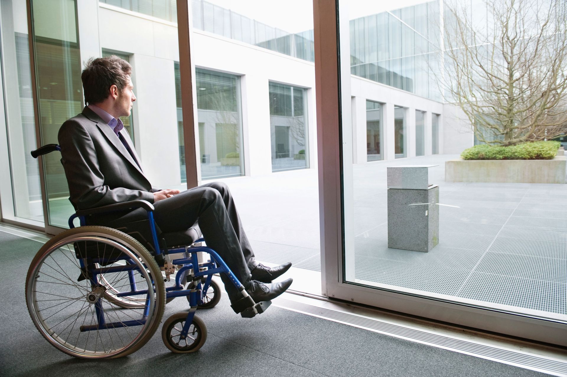 Man in wheelchair looking out a window, in a modern building.