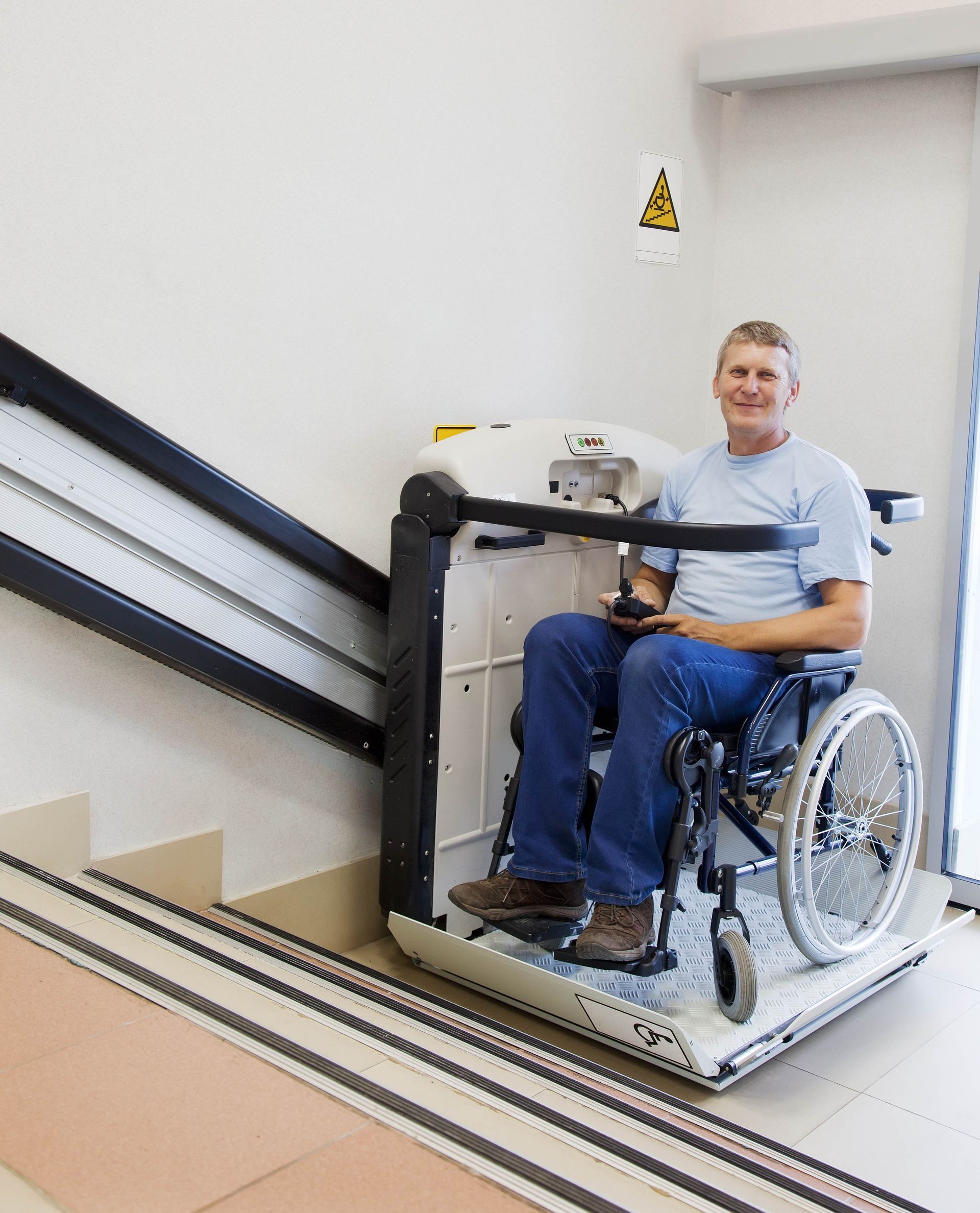 Man in wheelchair on a stair lift smiles. White, gray, and beige interior.