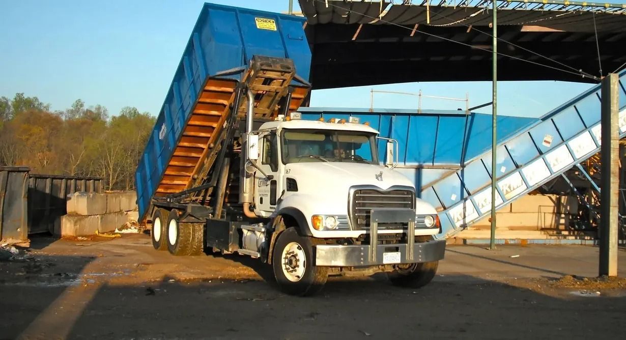 White roll-off truck dumping a blue container at a waste facility.