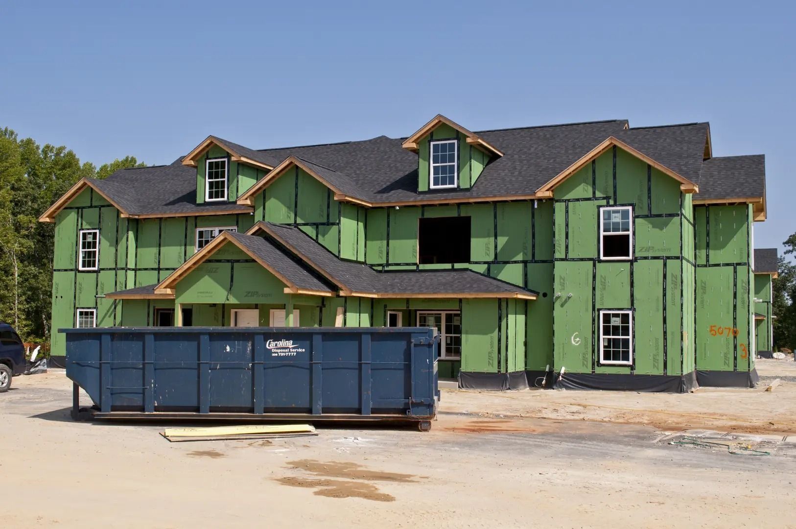 Building under construction with green sheathing, black roof, and a dumpster in front.