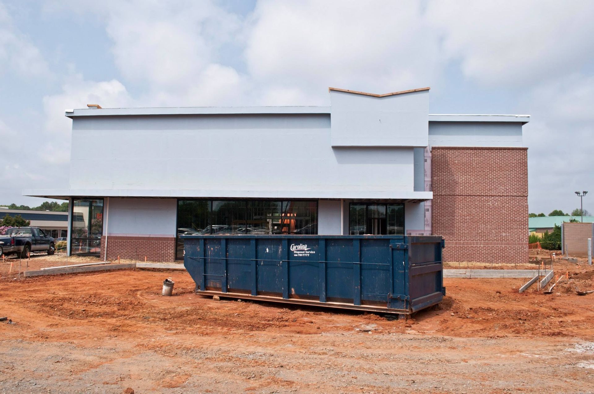 Exterior of a light blue building under construction, brown brick accents, dumpster in front.