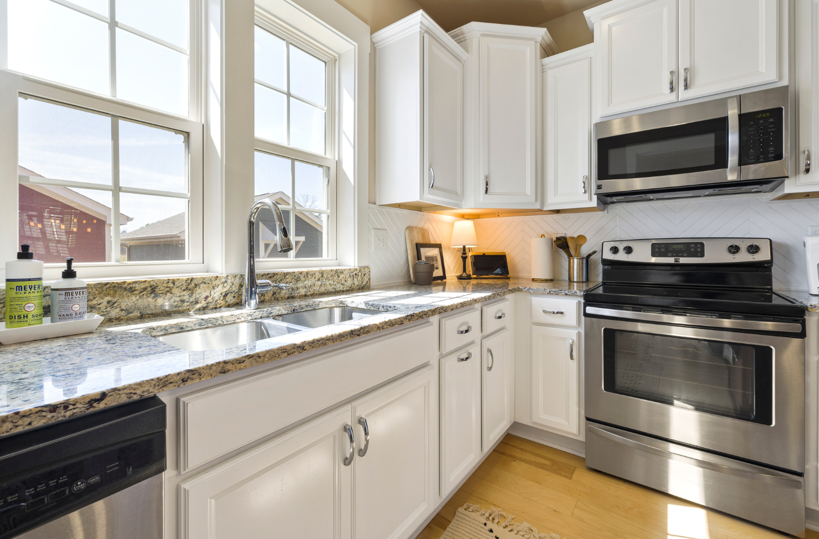 A kitchen with white cabinets, stainless steel appliances, granite counter tops and a sink