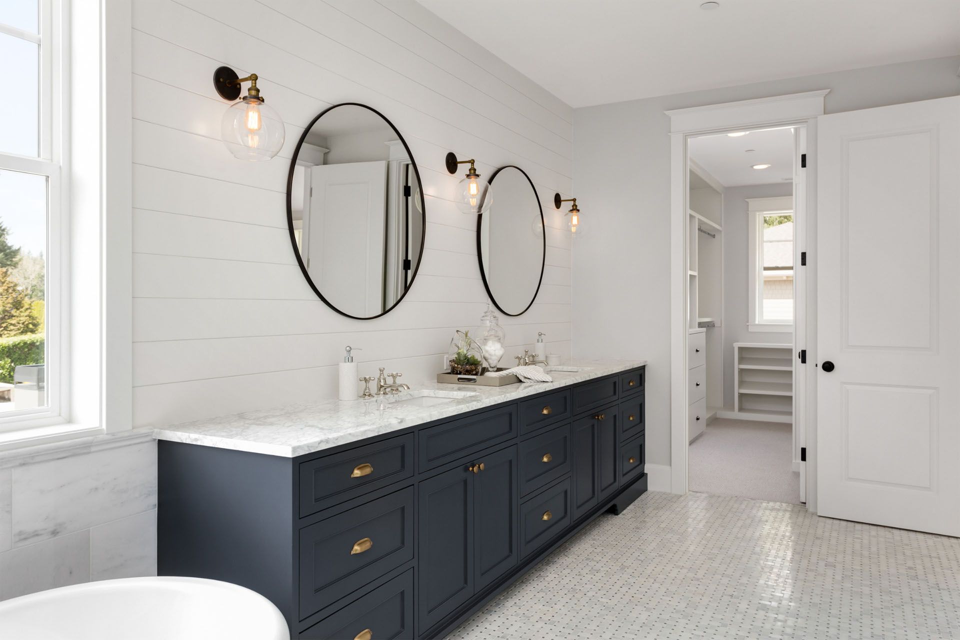 A bathroom with two sinks, two mirrors, a tub, and a walk in closet