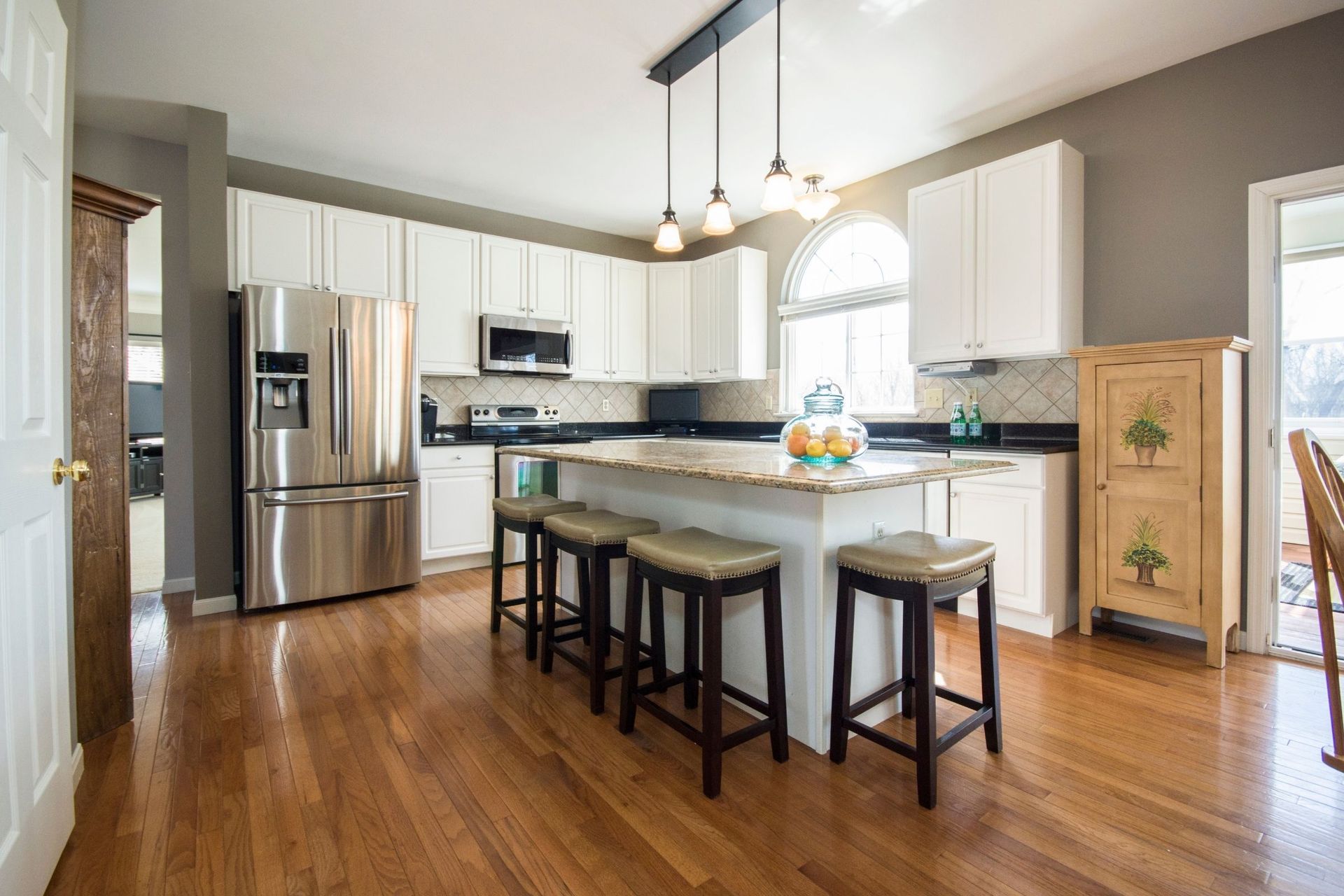 A kitchen with hardwood floors, white cabinets, stainless steel appliances and a large island