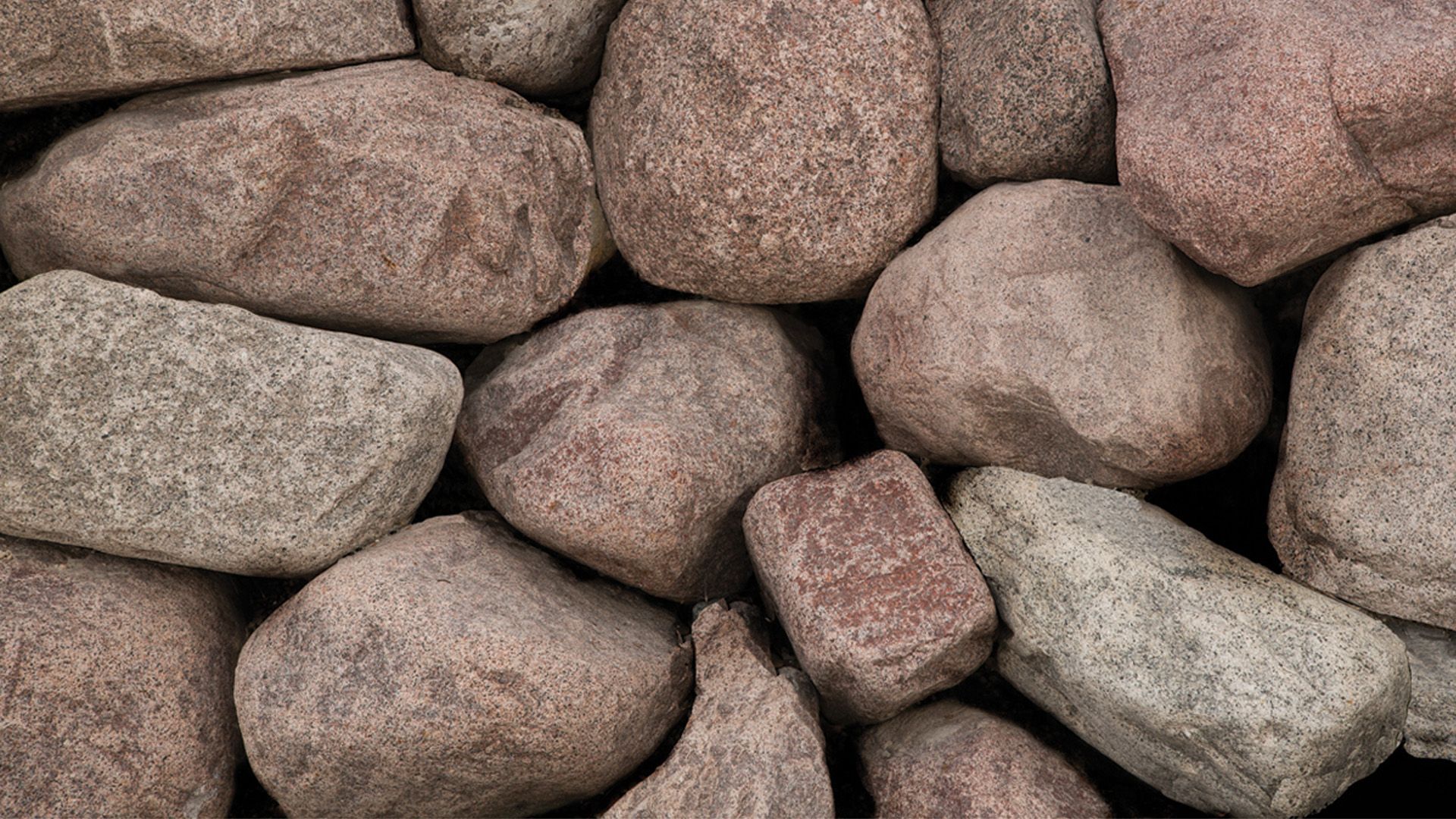 A close-up view of a pile of textured, weathered granite stones in shades of brown, tan, and gray.