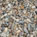 A close-up view of various small, rounded river rocks in shades of gray, brown, tan, and white.