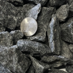 A US quarter coin rests on a pile of dark, jagged crushed stone gravel.