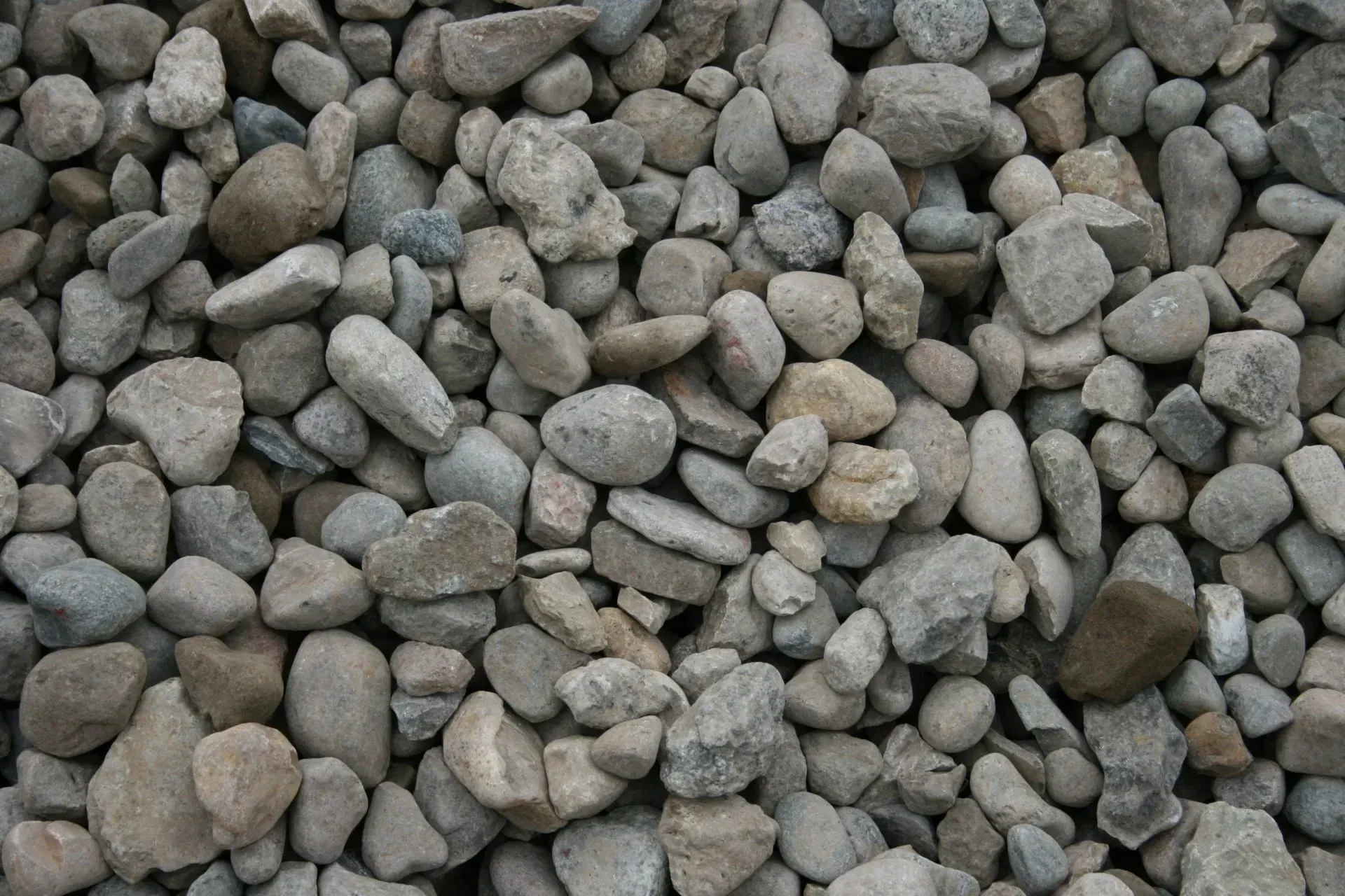 A close-up view of numerous rounded, grey and beige stones and pebbles of varying sizes packed closely together.