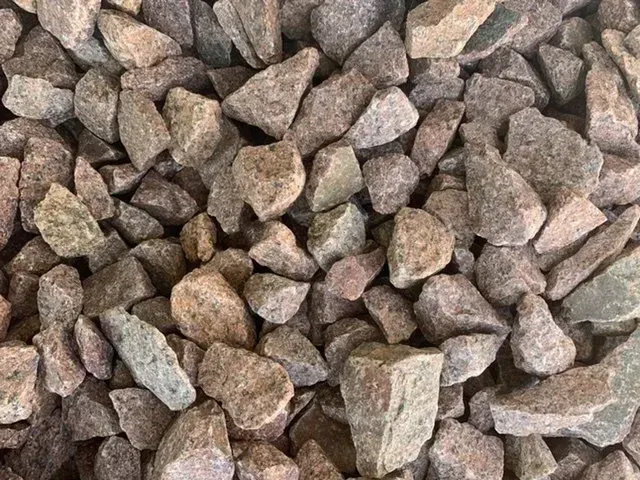 A close-up view of crushed granite or pinkish-brown landscaping gravel with angular, rough-textured stones.