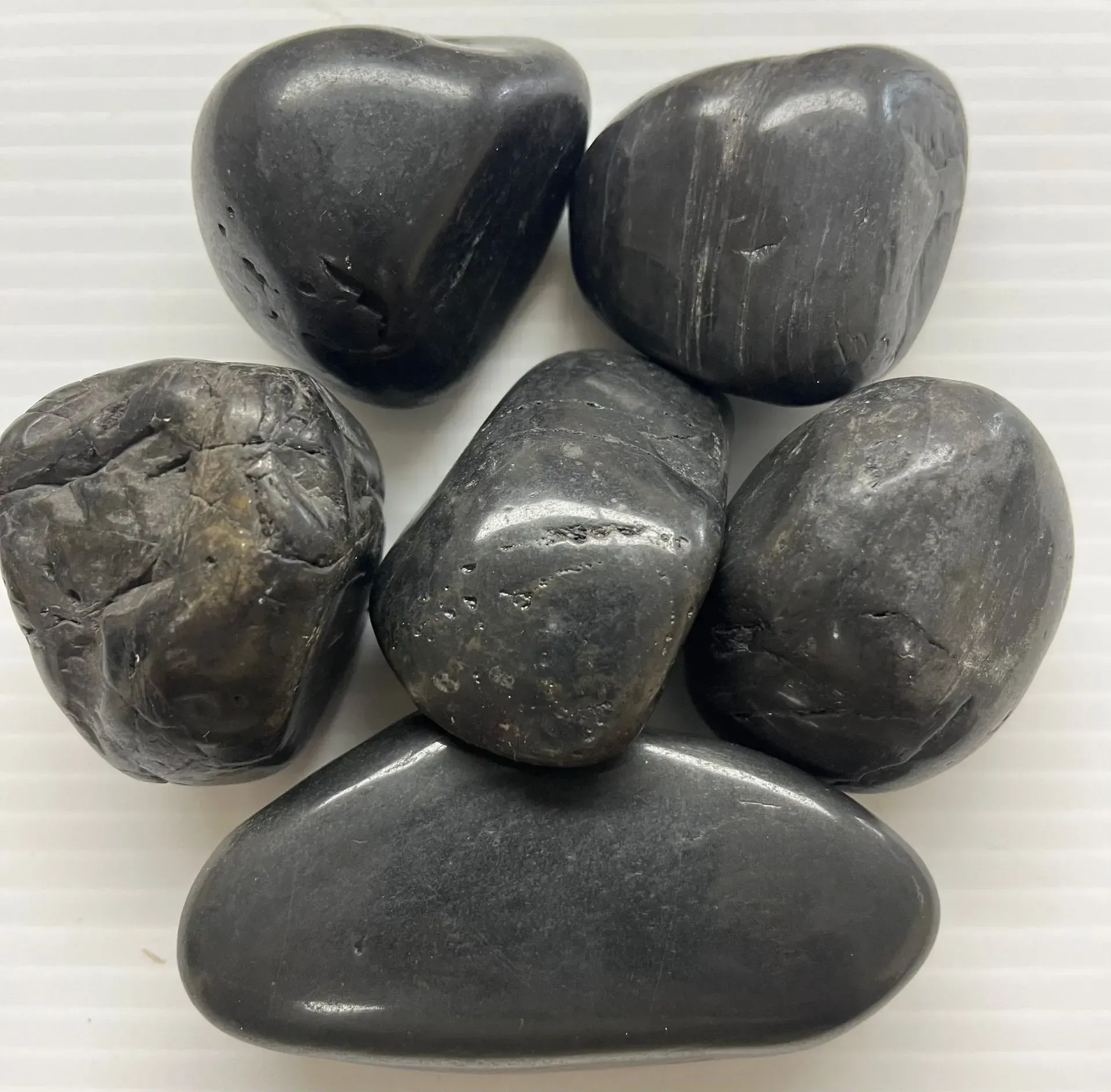 Six smooth, polished black river stones arranged against a white background.