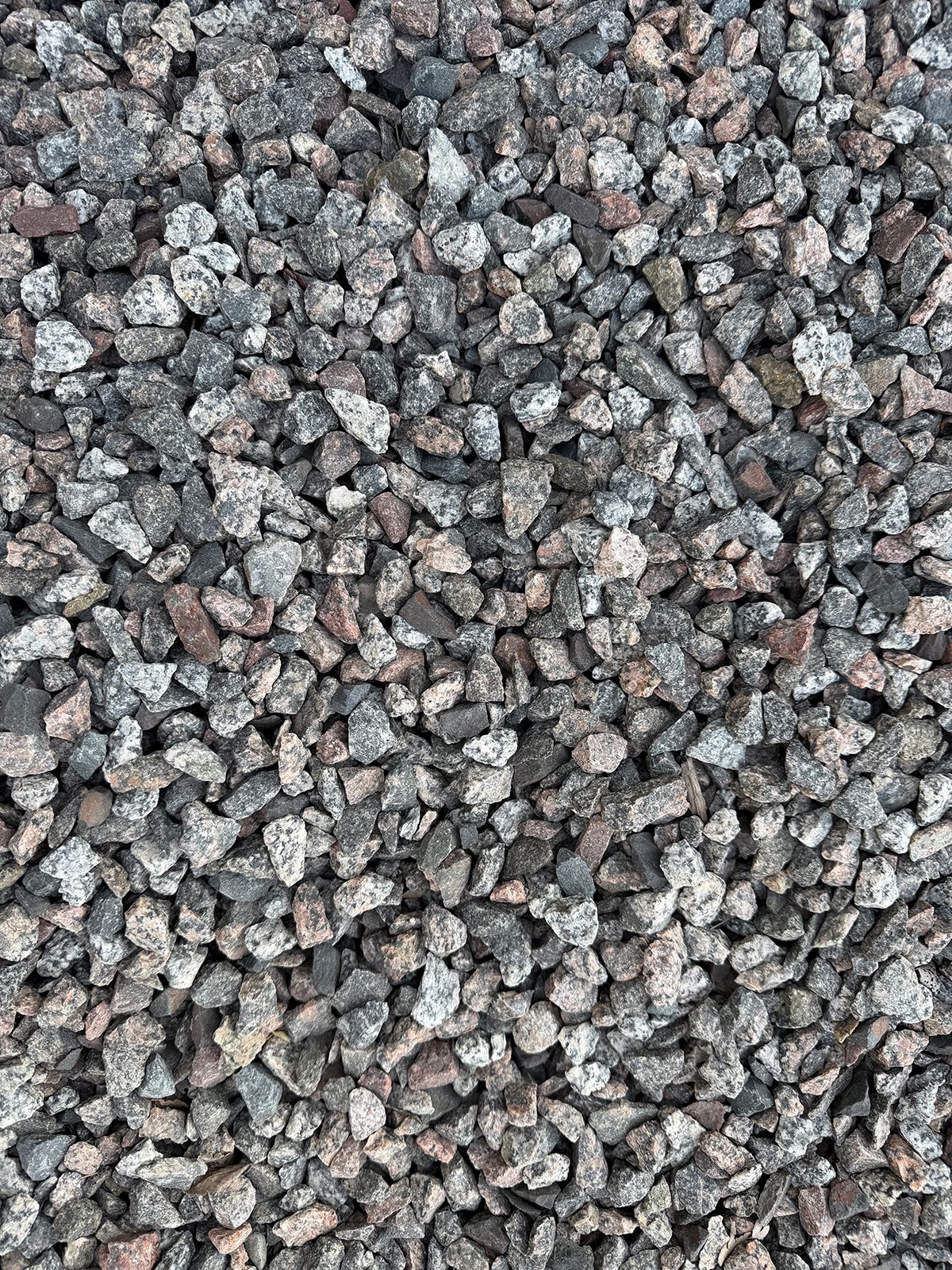 Close-up view of crushed granite gravel featuring a mix of grey, black, and pink-toned stone fragments.