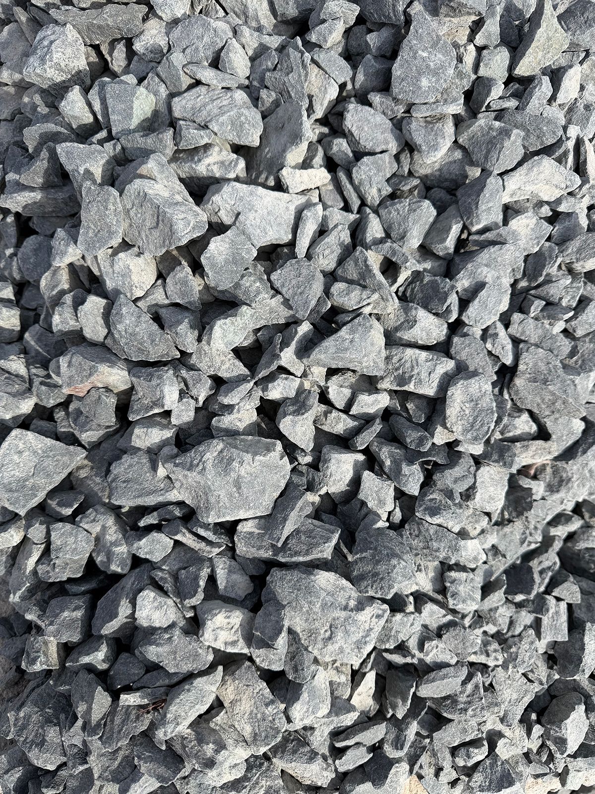 A close-up view of crushed dark gray gravel or stone aggregate with varied, angular shapes and sizes.