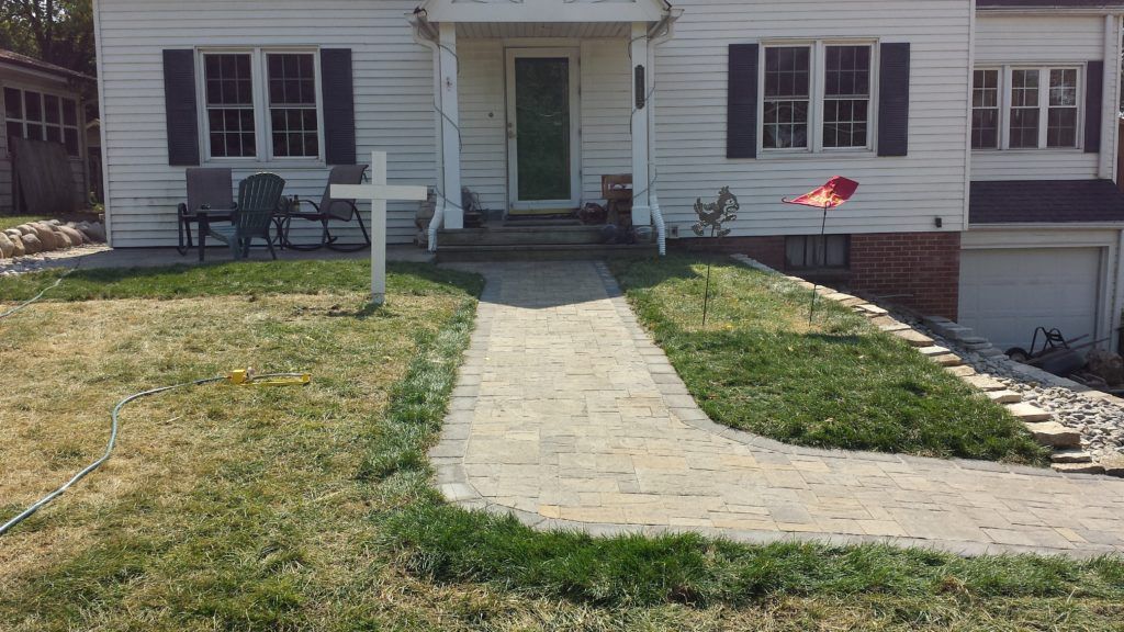 A house with a white exterior, blue shutters, and a newly installed paved walkway leading to the front porch.