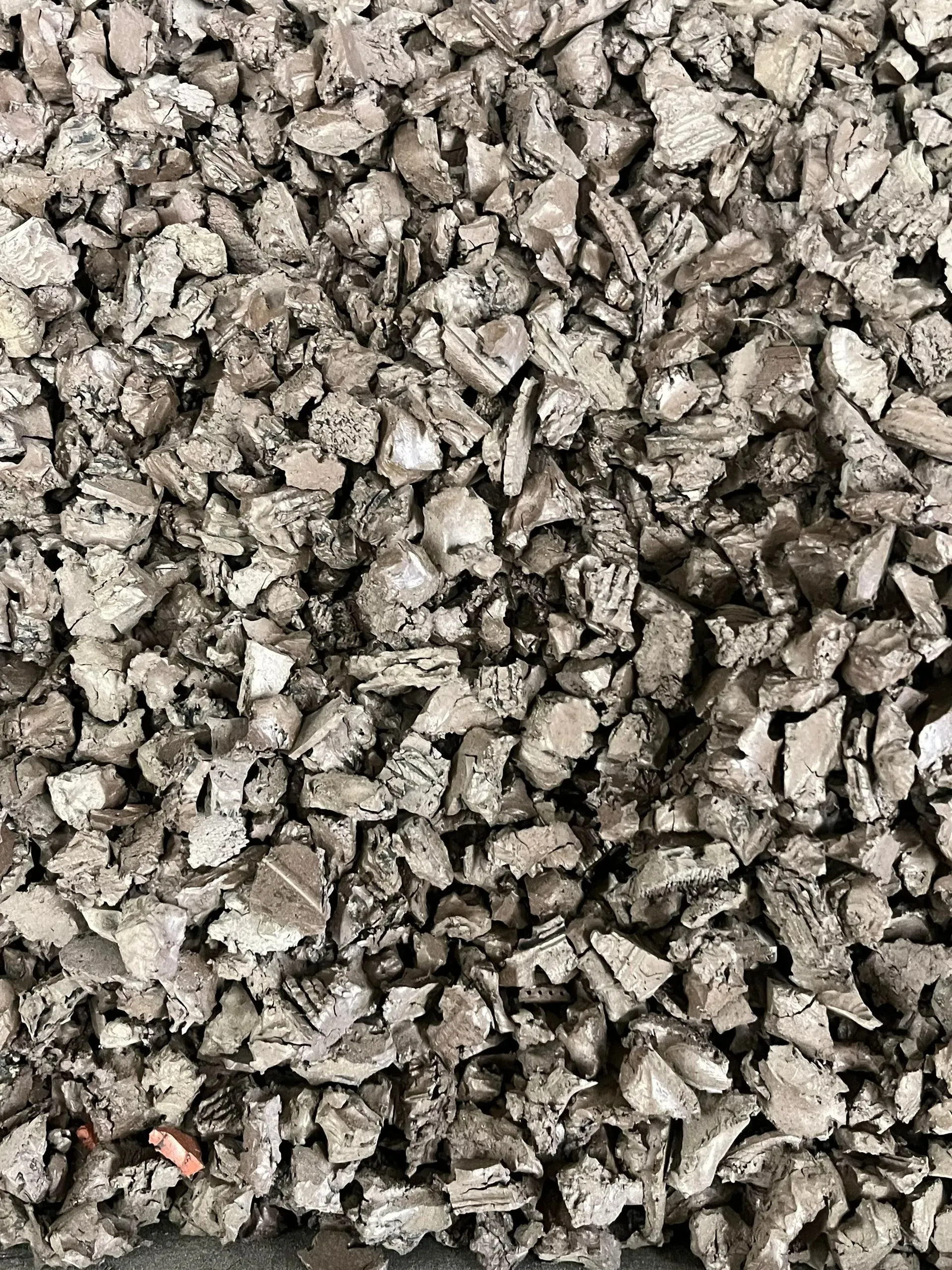A close-up of dark grey, coarse recycled rubber mulch or shredded rubber pieces.