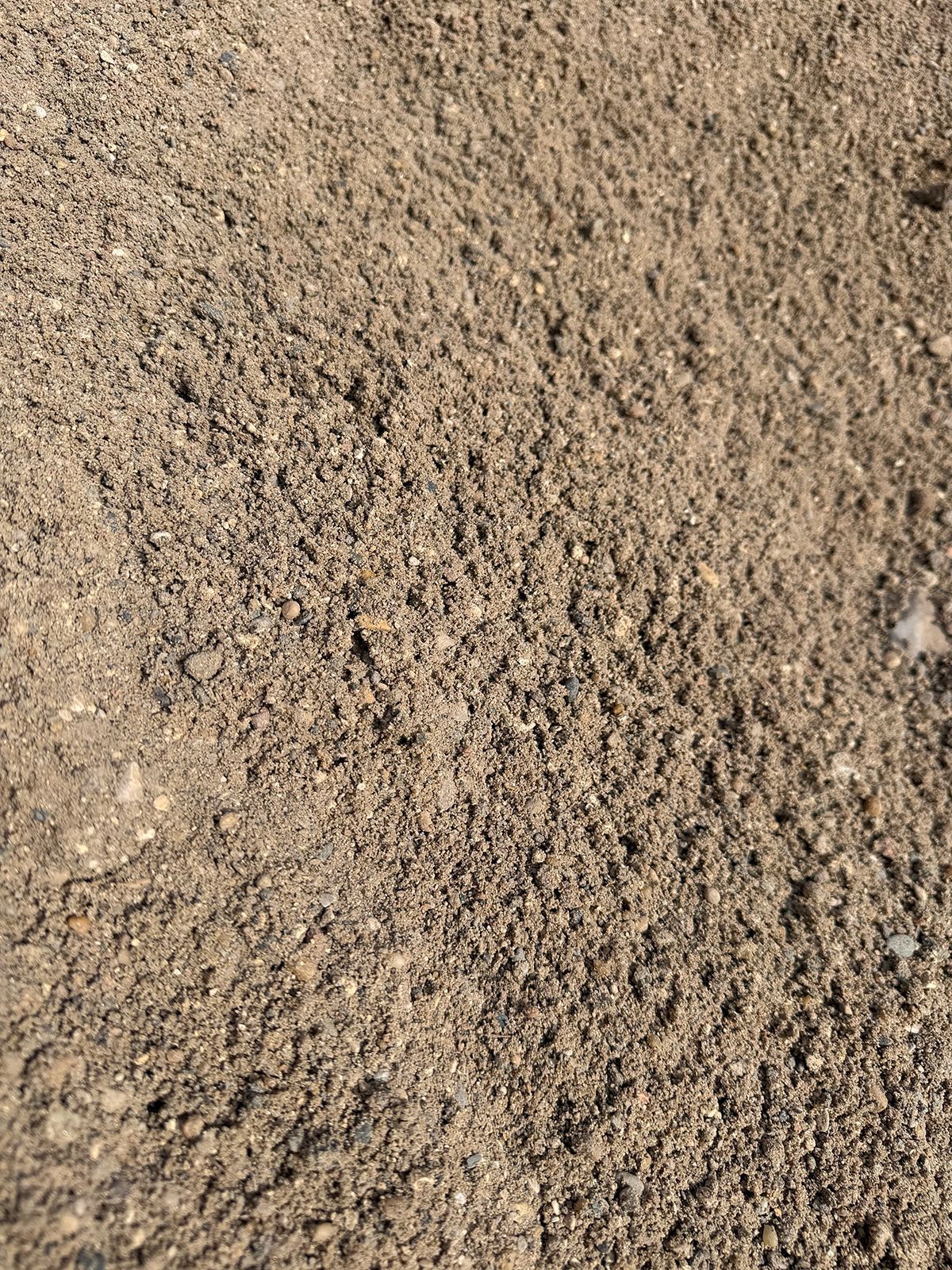 A close-up, top-down view of light brown, coarse sand or small gravel texture.
