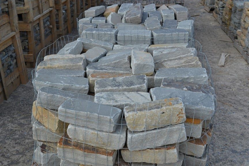 A wire crate filled with rectangular, rough-hewn grey and tan building stones stacked in an outdoor storage area.