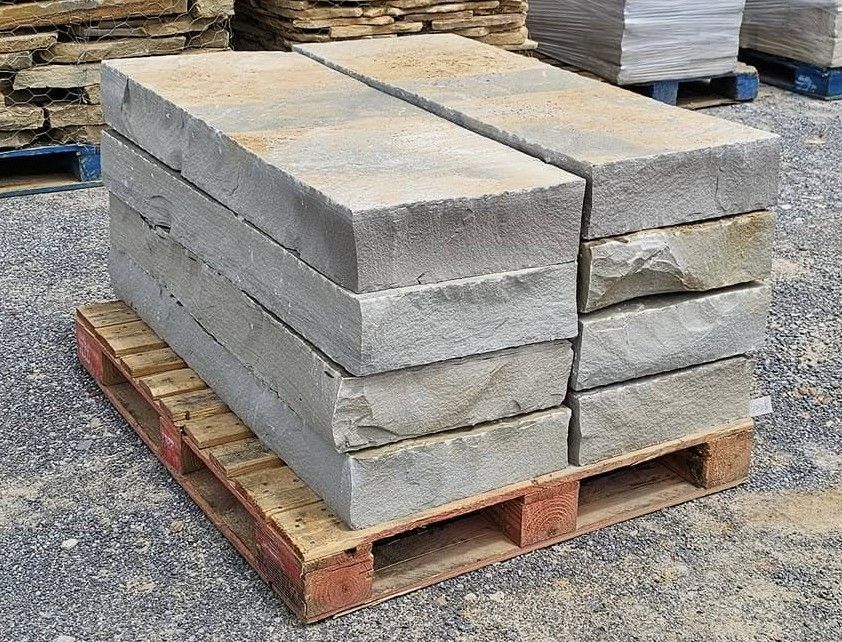 A pallet loaded with two rows of stacked, rectangular, gray natural stone blocks in an outdoor stone supply yard.