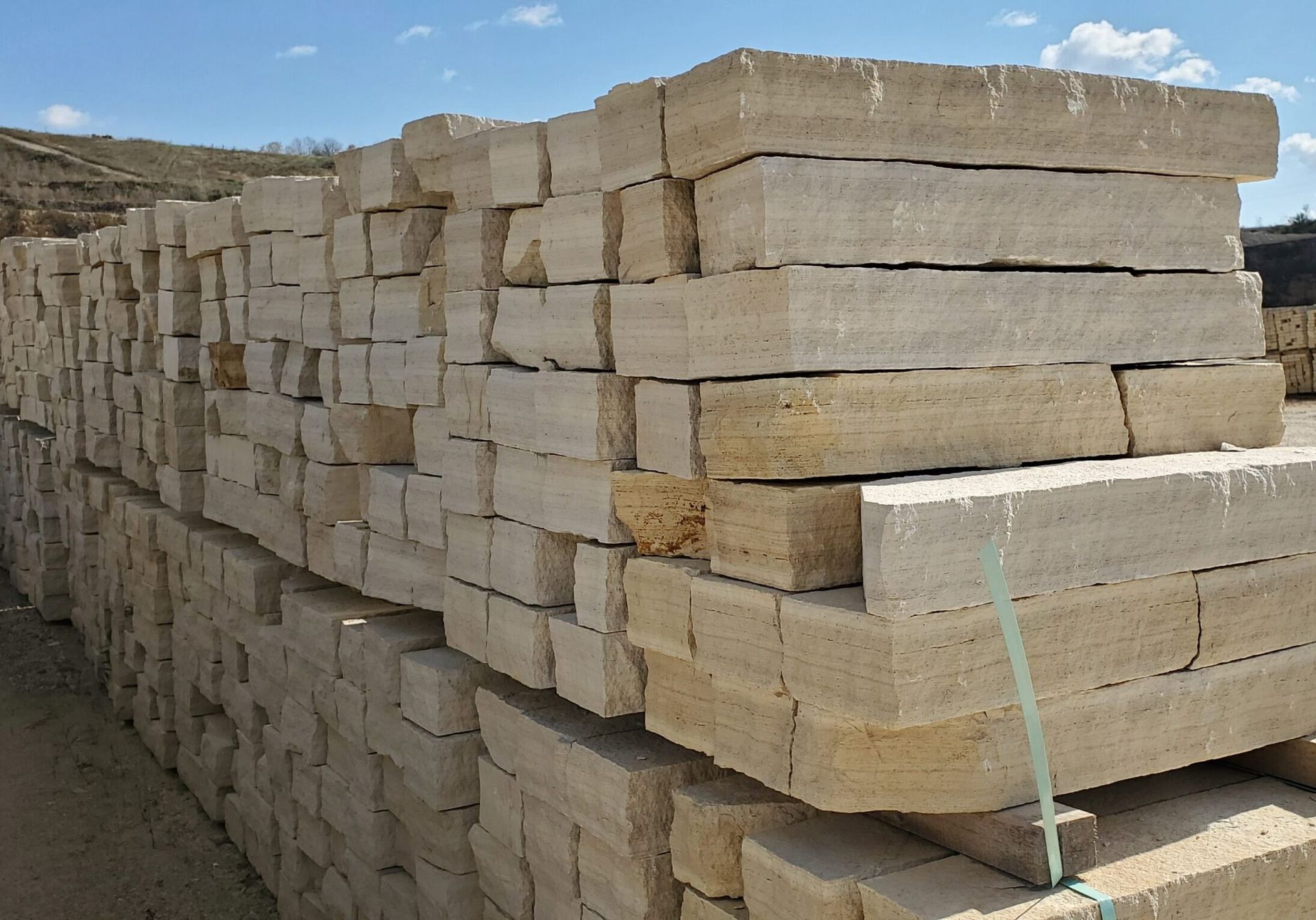 Stacked, rectangular beige limestone blocks arranged in neat rows in an outdoor storage yard under a blue sky.