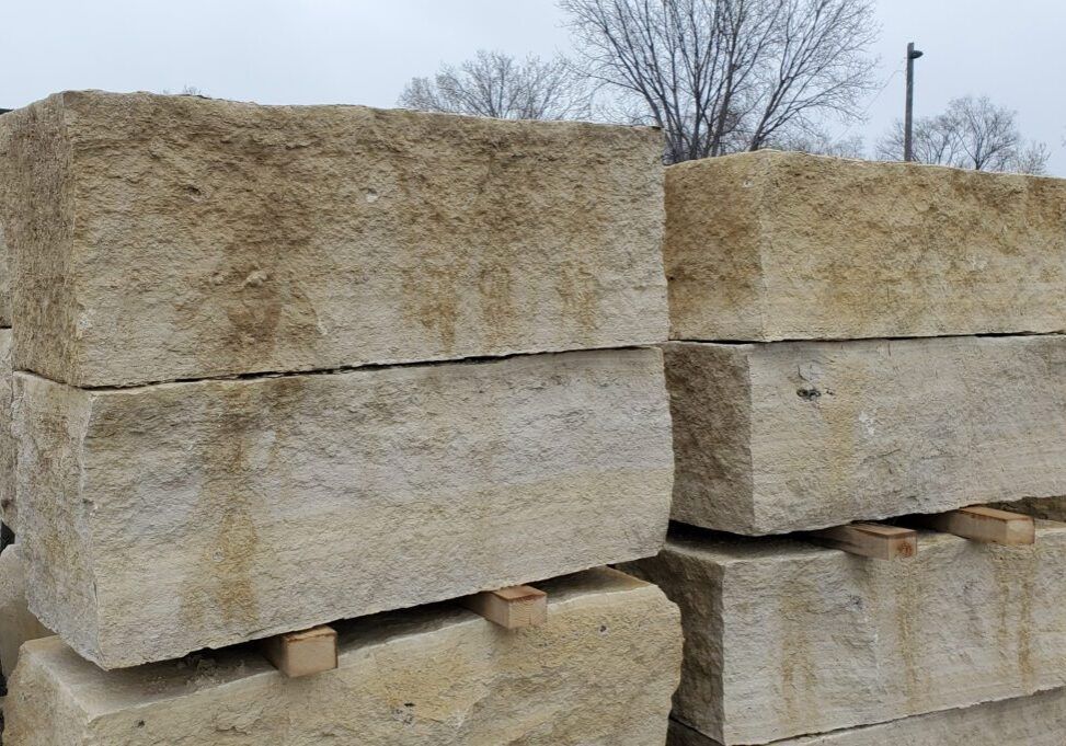 Stacked, rough-hewn rectangular blocks of beige limestone resting on wooden spacers outdoors.