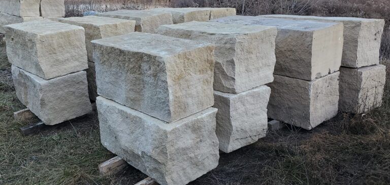 A stack of rectangular, light-tan natural stone blocks resting on wooden pallets in an outdoor field.