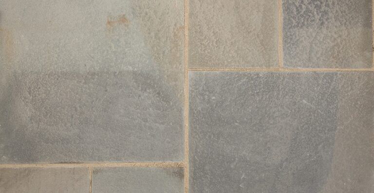 A close-up view of a floor paved with large, rectangular, multi-toned gray stone tiles with thin, light-colored grout lines.