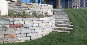 Stone retaining walls with built-in stairs leading to a house, set in a grassy yard.