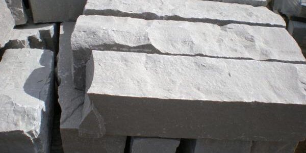 A stack of rectangular, light grey cut stone blocks with rough, textured front faces.