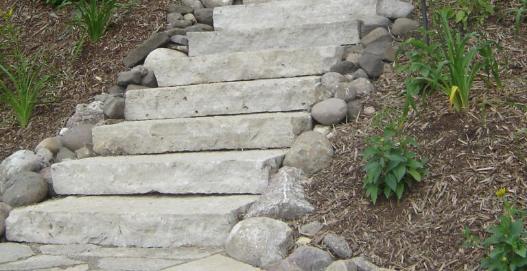 Stone steps built into a landscaped hillside, framed by border rocks and small plants.