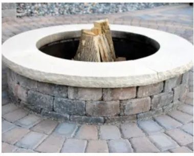A circular stone fire pit with a light beige stone rim and a brick base, containing a small stack of firewood.