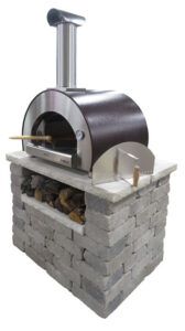 A dark-domed wood-fired pizza oven with a metal chimney, mounted on a rustic grey stone base with firewood storage.