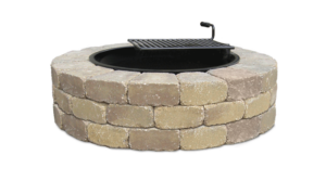 A round fire pit built with stacked, tan-colored stone blocks, featuring an integrated black metal cooking grate.