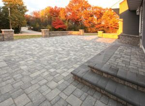 A gray paver patio with stone steps and retaining walls, set against a background of autumn trees with vibrant foliage.