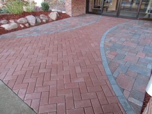 Curved red brick walkway with a gray border leading to a building entrance.