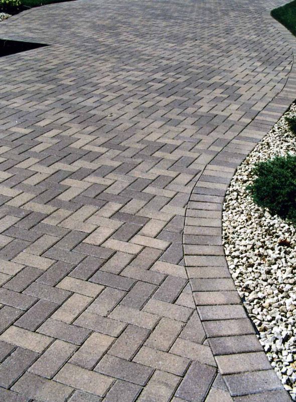Curved brick paver walkway beside a gravel border and green grass