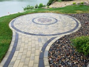 Circular stone patio with a spiral border beside a grassy waterfront path