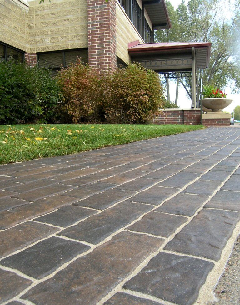 Stone walkway leading to a house entrance with shrubs and a covered porch