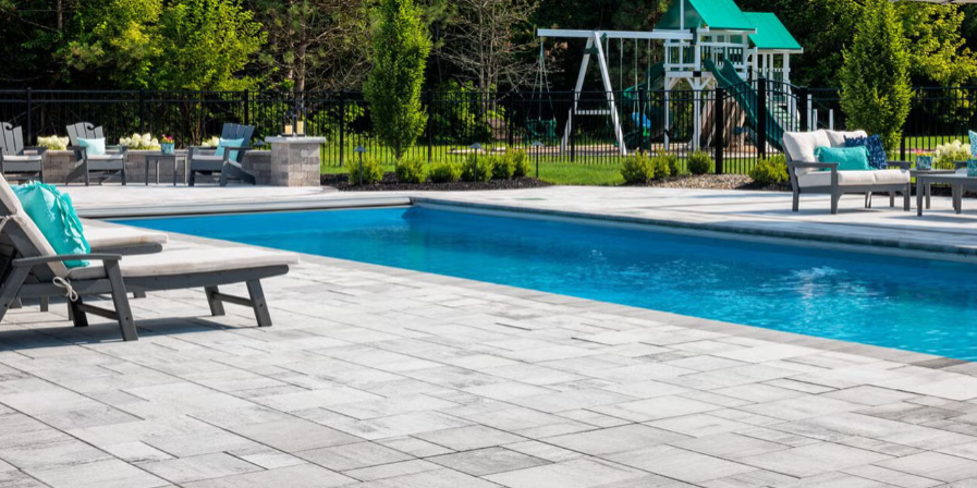 Outdoor swimming pool with blue water, lounge chairs, and a patio under clear daylight
