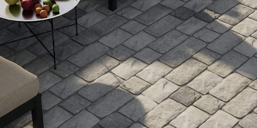 Gray stone patio with sunlight, a beige chair, and a small table holding fruit.
