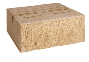 A tan, rectangular concrete landscaping block with a rough, split-face front texture and a flat top.